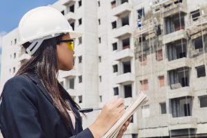 african-american-lady-safety-helmet-writing-notepad-near-building-construction
